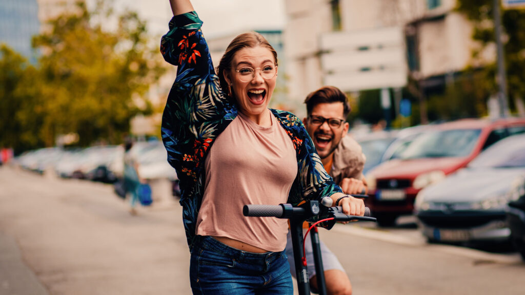 Young couple having fun driving electric scooters through the city